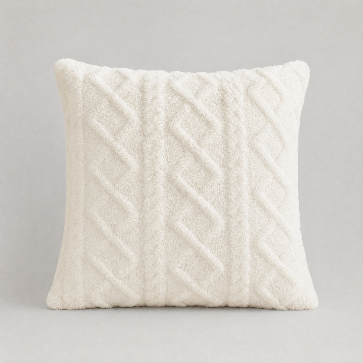 Cream cable knit plush cushion cover seen from the front on a light grey background