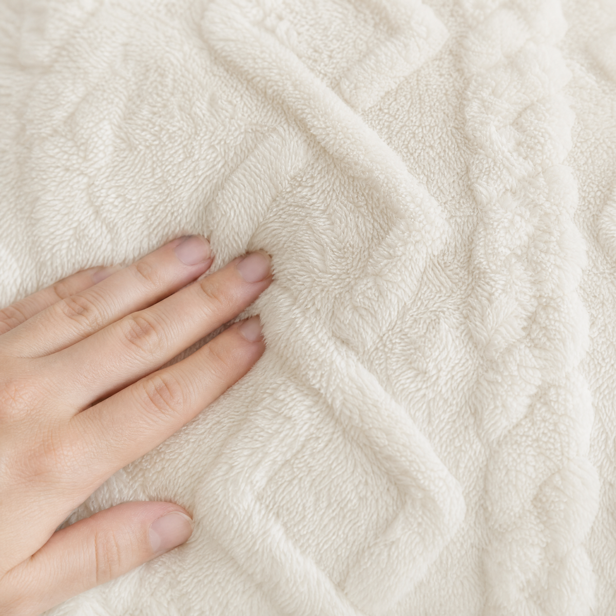 Hand pressing into the raised cable pattern of the cream plush cover