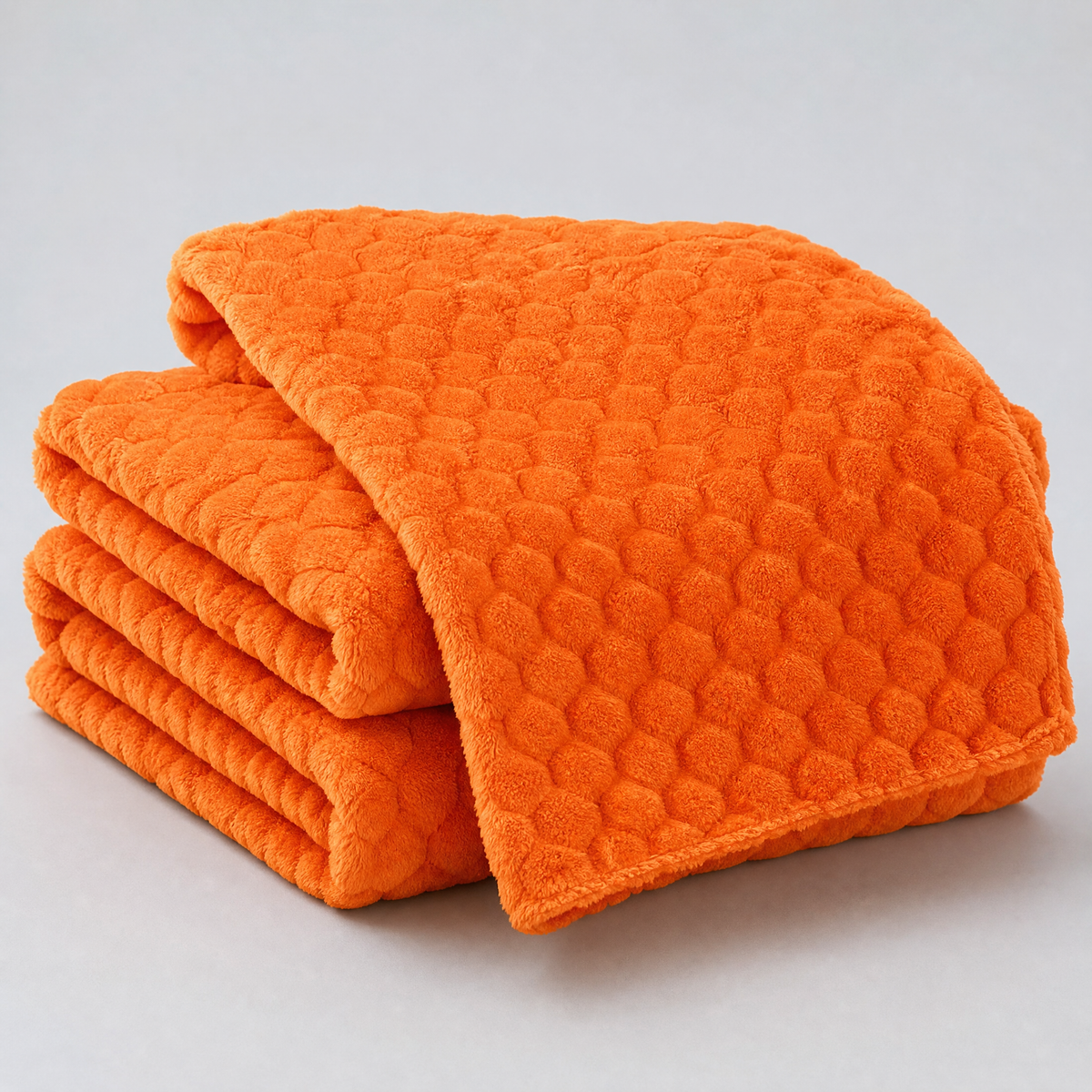 Warm Orange honeycomb velvet couch cover, folded, on a light grey background
