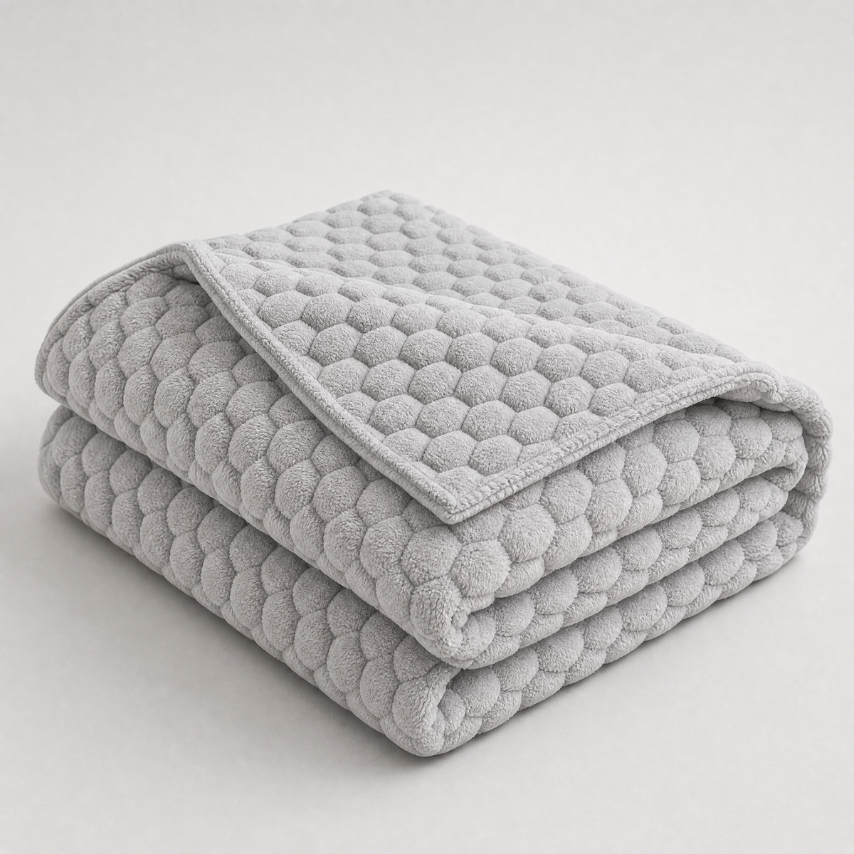 Grey honeycomb velvet couch cover, folded, on a light grey background