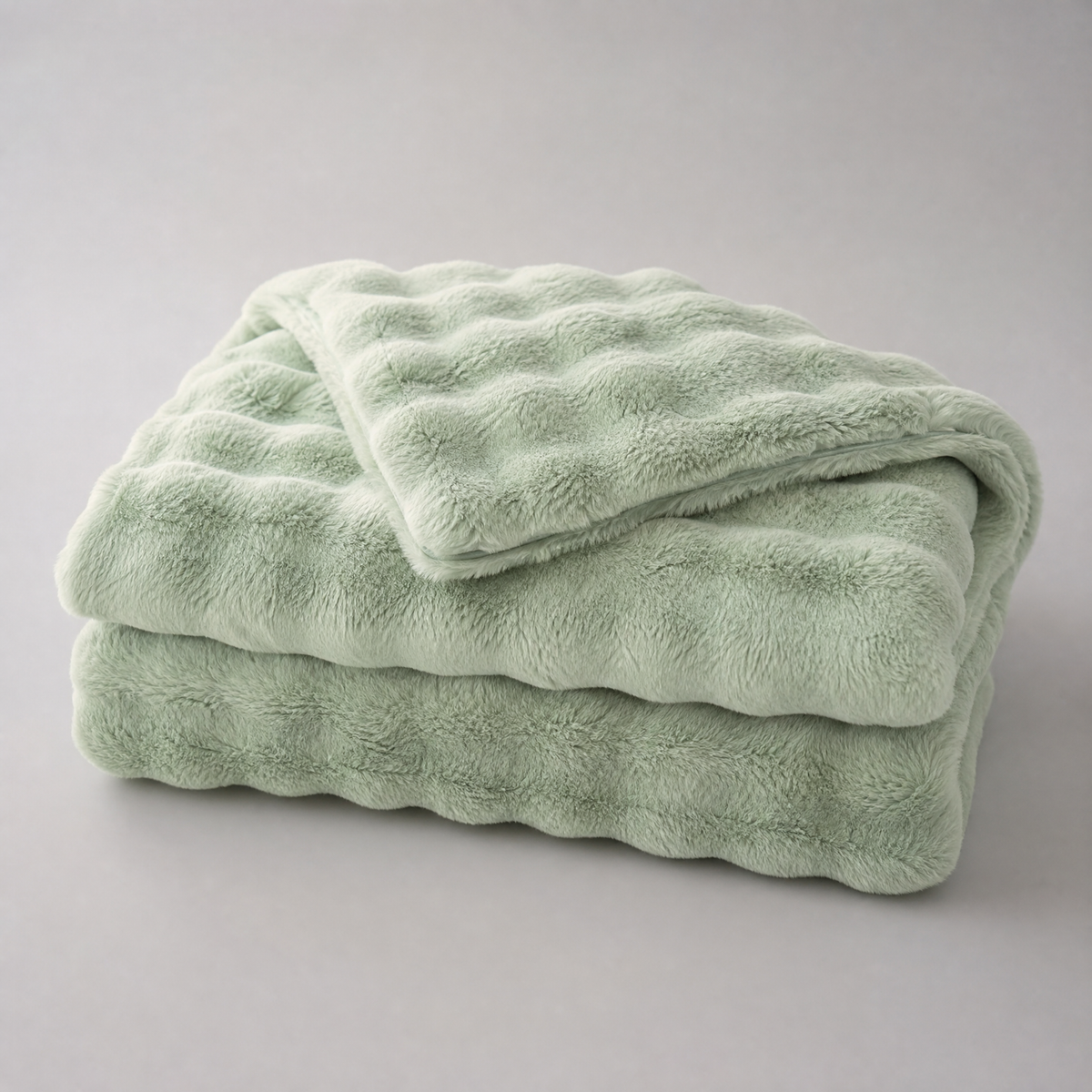 Sage Green quilted faux fur couch cover, folded, on a light grey background