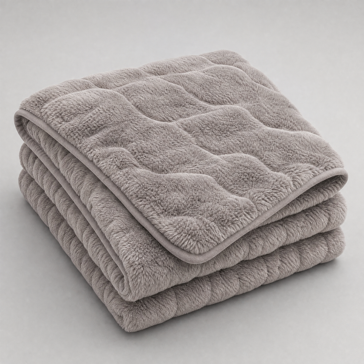 Grey quilted faux fur couch cover, folded, on a light grey background