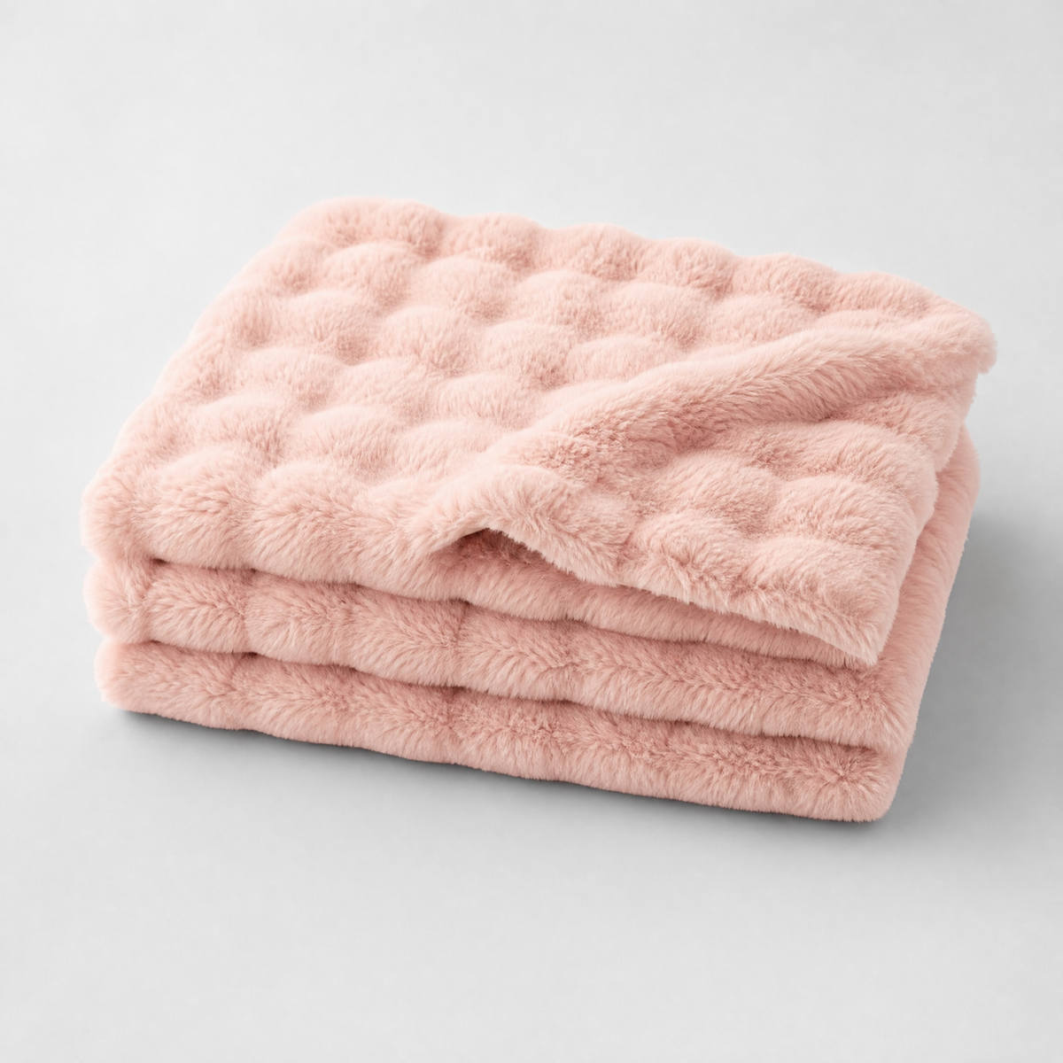 Blush Pink quilted faux fur couch cover, folded, on a light grey background