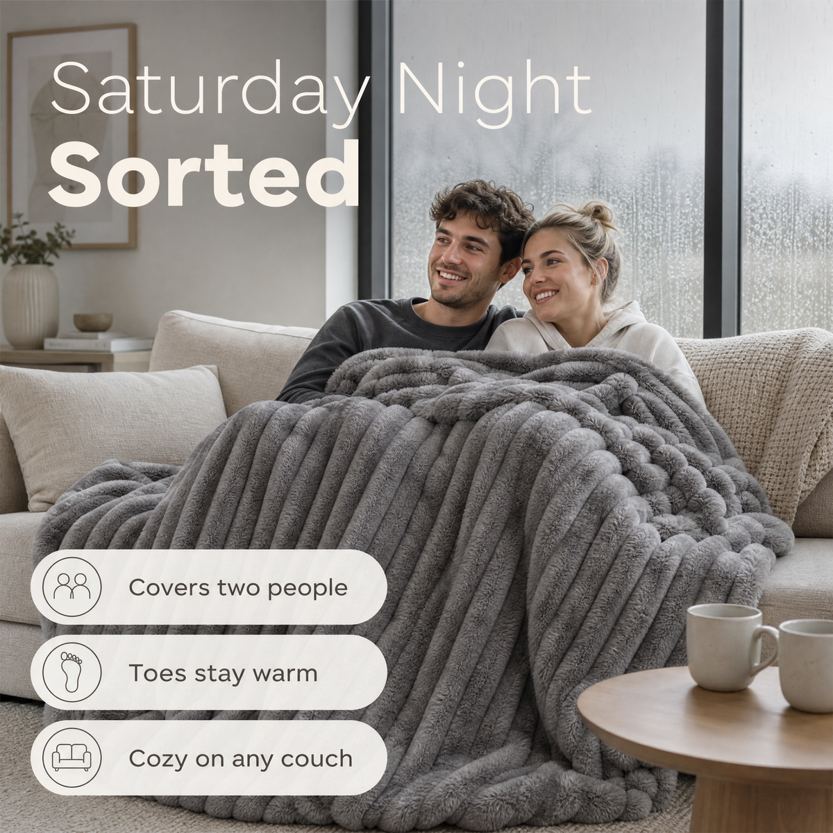 Couple on a couch under one grey rib plush blanket, feet tucked in
